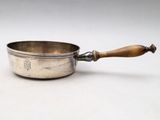 une vieille casserole en argent avec un manche en bois, posée sur une surface blanche