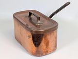 une petite casserole en cuivre avec une poignée, posée sur une surface blanche