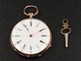 une montre de poche en or et une clé posées sur une surface noire