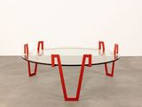 a round glass table with red legs and a glass top