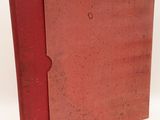 an old book with a red cover sitting on top of a white surface