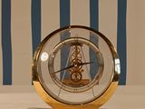 a gold clock sitting on a table with a blue and white striped wall behind it