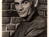 an old black and white photo of a man in a suit leaning against a brick wall