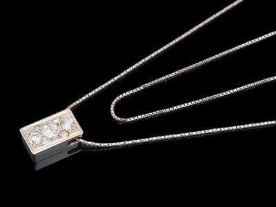 un gros plan d'un pendentif en diamant suspendu à une chaîne, sur fond noir