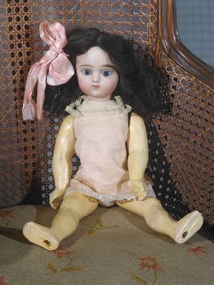 a small doll sitting on a chair with a pink bow on its head