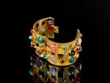an image of a gold bracelet with multi colored stones on a black surface