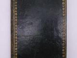 a black book with gold trim sitting on top of a white surface