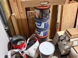 several buckets of paint are sitting on the floor next to a pile of wood