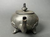 an old silver teapot with a lid on a gray surface