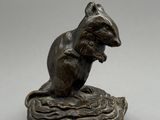 une statue en bronze représentant une souris assise sur un morceau de bois
