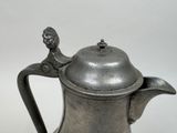 a silver coffee pot with a handle on a table