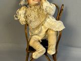 une petite poupée assise sur une chaise, coiffée d'un chapeau
