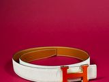 a white belt with a gold h buckle on a pink background