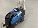 un homme vêtu d'une salopette blanche, debout à côté d'une machine bleue dans un entrepôt