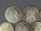 six different types of silver coins on a gray surface