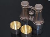 three silver cups and a pair of binoculars on a black table