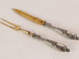 pair of silver plated knives with a gold handle on a white surface