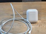 Des AirPods d'Apple sont posés sur une table en bois, à côté d'un chargeur