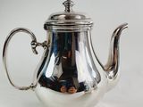a silver tea pot with a handle on a white surface