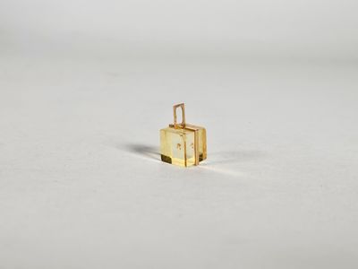 petite breloque en forme de valise dorée sur une surface blanche, avec un fond blanc