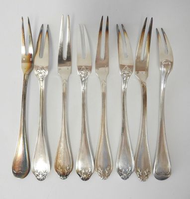 six forks and a knife are lined up on a white surface