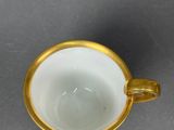 a white cup with a gold rim next to a spoon
