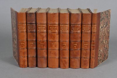 six old books are lined up in a row on a gray surface