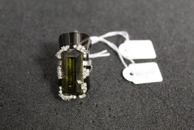 une photo d'une bague en tourmaline verte et diamants posée sur un fond noir