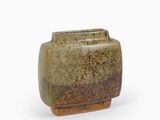 un vase vert au pied marron posé sur une surface blanche