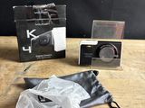 une photo représentant un appareil photo et un sac posés sur une table en bois