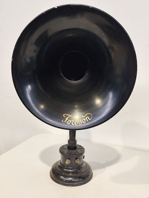 un vieux gramophone noir posé sur un support, devant un fond blanc