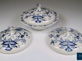 Trois plats bleus et blancs avec leurs couvercles sont posés sur une table