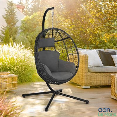 une chaise suspendue noire sur une terrasse en bois dans un jardin