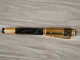 the pen is laying on the wooden table with a black and gold finish