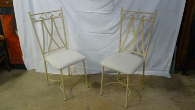 pair of white metal chairs with upholstered cushions in front of a white backdrop