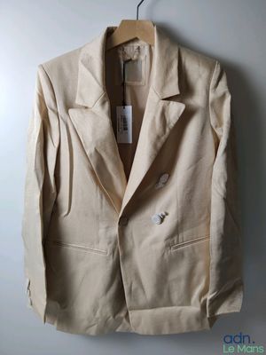une veste beige suspendue à un cintre sur un mur blanc