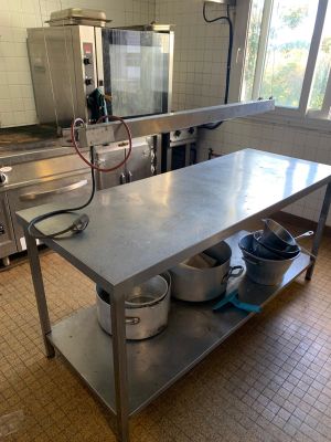 une grande table en acier inoxydable sur laquelle sont posés des casseroles et des poêles