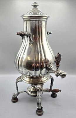 une cafetière ancienne en argent posée sur un socle, sur fond gris