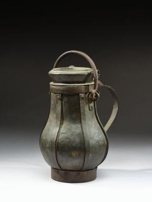 une image représentant un vase vert muni d'une anse, posé sur une surface blanche