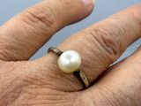 a person ' s hand holding a ring with a pearl on it