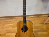 une guitare acoustique posée sur un parquet, près d'un mur