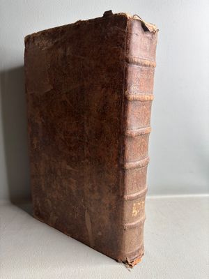 an old brown book sitting on top of a table next to a white wall