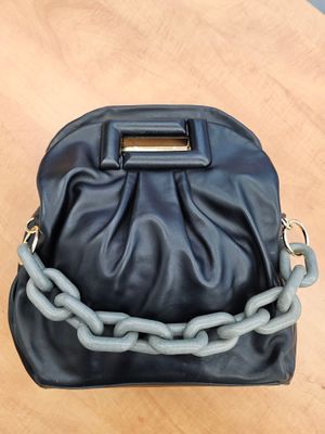 un sac à main noir et gris, entouré d'une chaîne, posé sur une table en bois