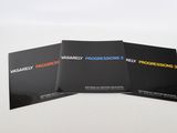 trois brochures noires posées sur une surface blanche, sur fond blanc