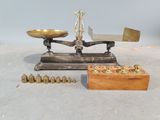 une balance ancienne avec des poids en laiton et un coffret en bois, posée sur une surface blanche