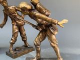 three bronze figurines of men with guns on a table