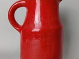 un vase rouge muni d'une anse, posé sur une table