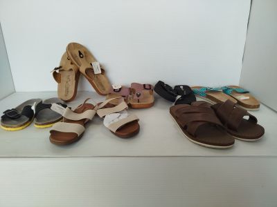 Plusieurs paires de sandales sont alignées sur une étagère devant un mur blanc