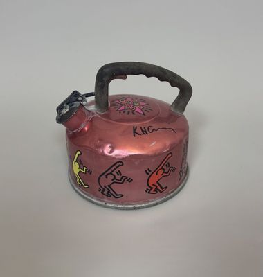 a pink tea kettle with graffiti on it on a white surface
