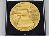gold plated medal with a car and a woman in a dress